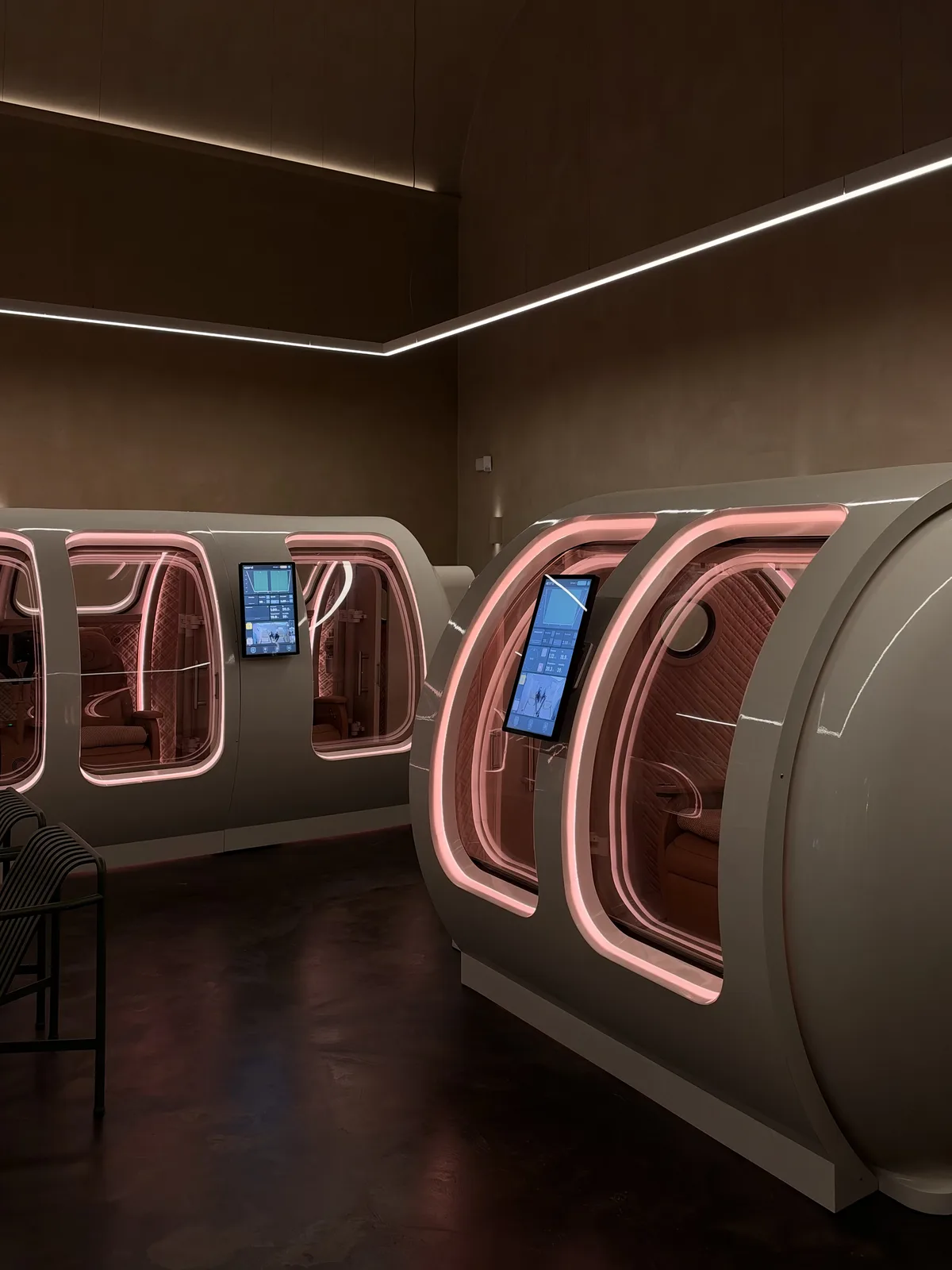 Two hyperbaric chambers with soft pink lighting in a dim clinic room