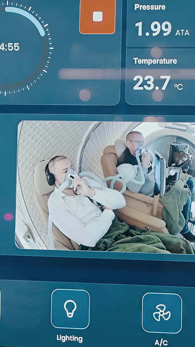 Two guests breathing through oxygen masks in adjacent chamber seats during a morning session